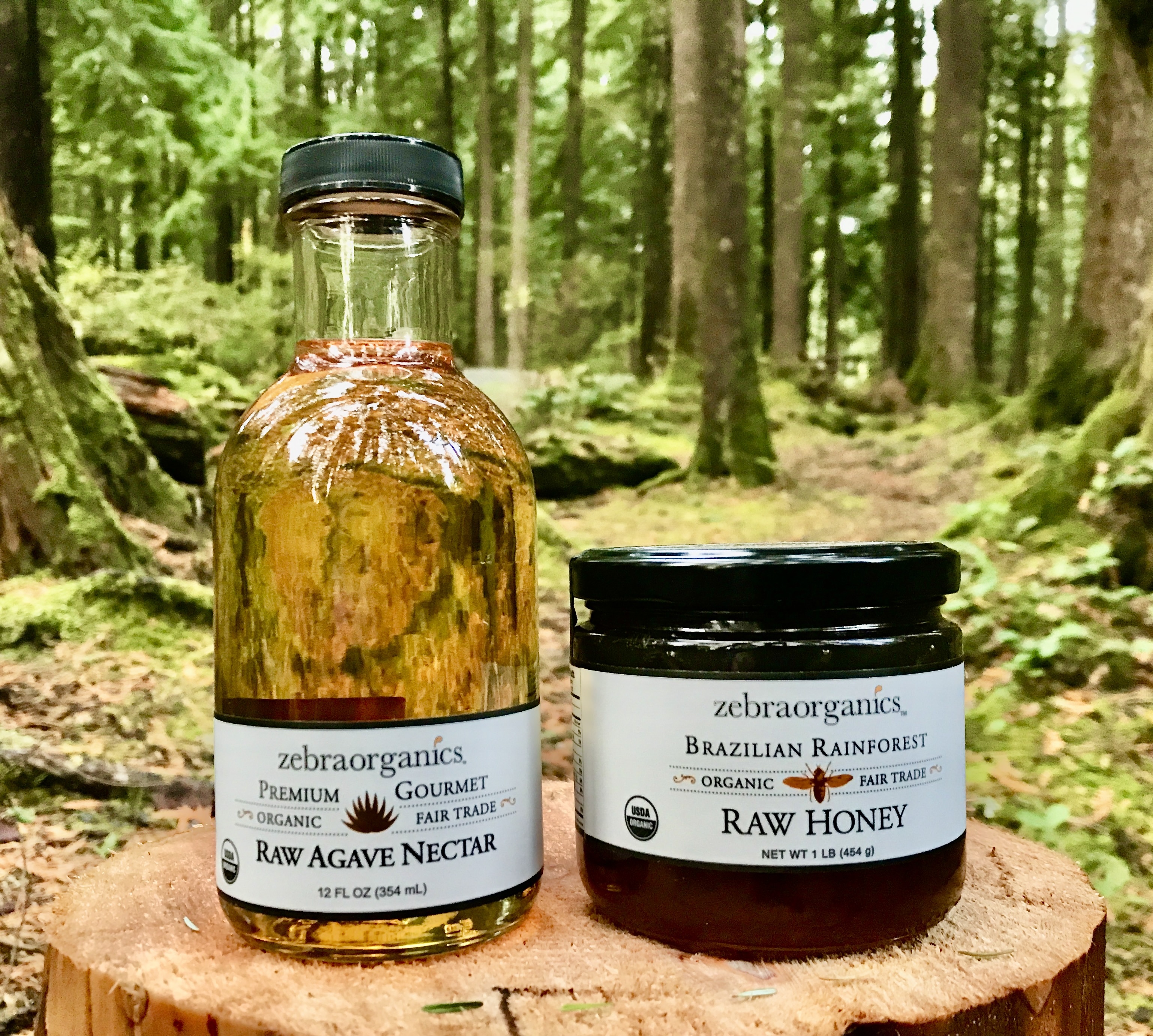 jar of organic agave and jar of organic honey, on a log in the forest